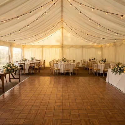 Mise en situation : piste de danse en teck au centre d'un chapiteau de mariage aux guirlandes lumineuses